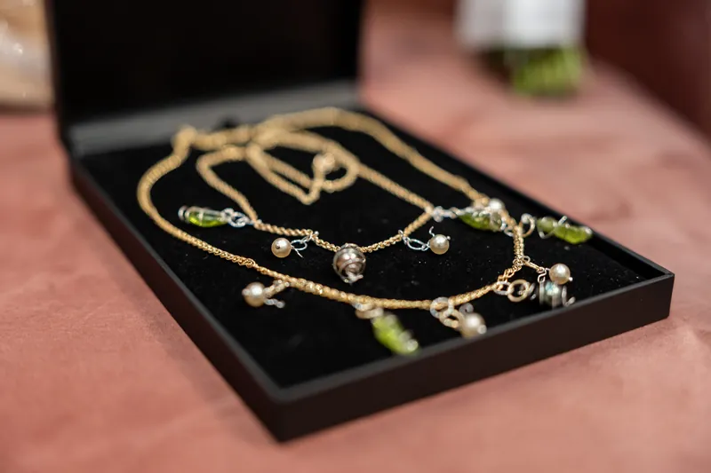 Gold chain necklaces with gemstone pendants are displayed on a black jewelry tray against a rose-colored surface.