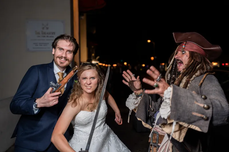 Chris and Sybil pose with a pirate-costumed character outside The Treasury on the Plaza, all three grinning at the camera
