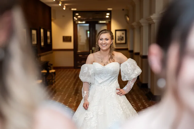 Sybil poses in her white off-shoulder wedding dress with puffed sleeves down a softly lit hallway at The Treasury.