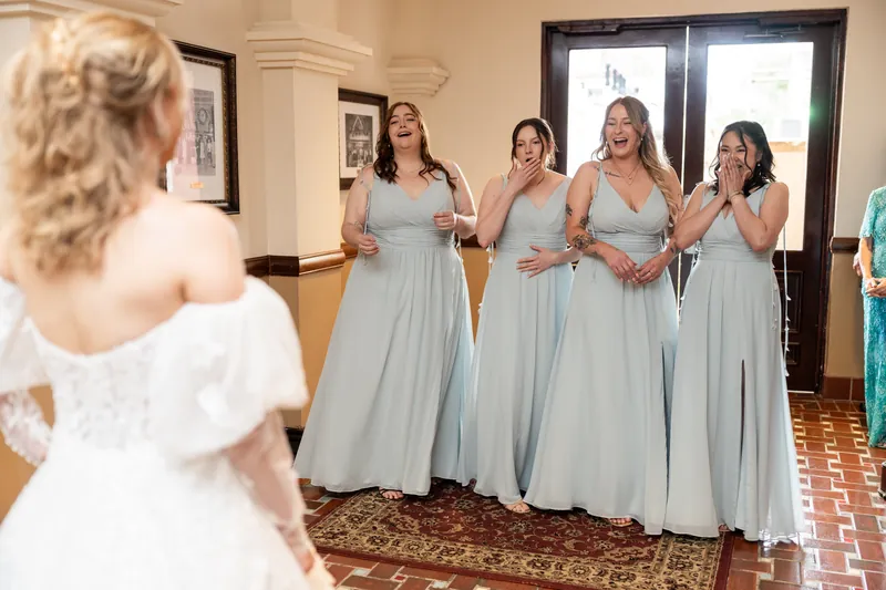Sybil in white faces four attendants in pale blue dresses during a first look moment at The Treasury on the Plaza.
