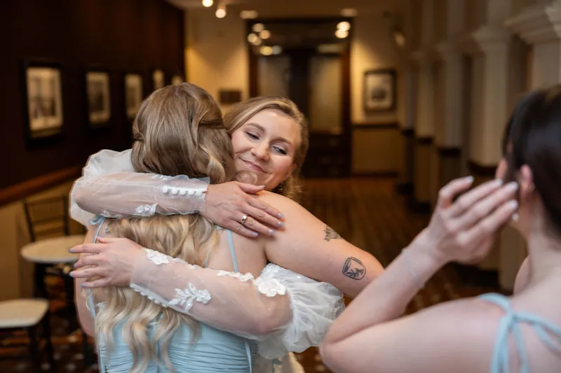 Sybil embraces someone in a light blue dress while another attendant reaches toward them in an emotional embrace.