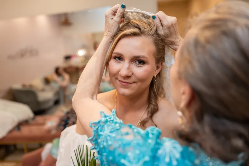 Someone adjusts Sybil's hair while she grins at the camera during getting-ready preparations.