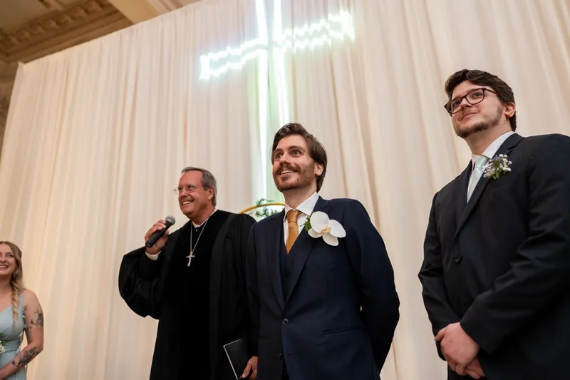 Three men in suits stand together under dramatic uplighting during the ceremony.