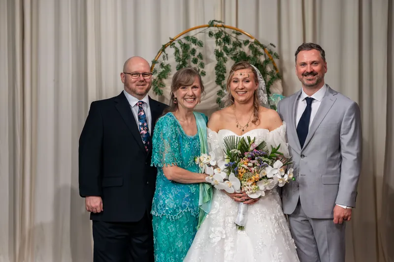 Sybil poses with three family members in front of the greenery arch, all dressed formally for the occasion.