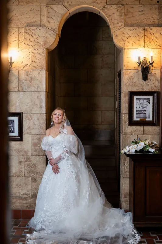 Sybil stands alone in her lace gown and veil beneath The Treasury's arched doorway, train trailing behind her.