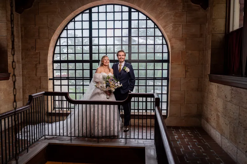 Sybil and Chris stand together at The Treasury's arched window, looking out over the venue's architectural details.