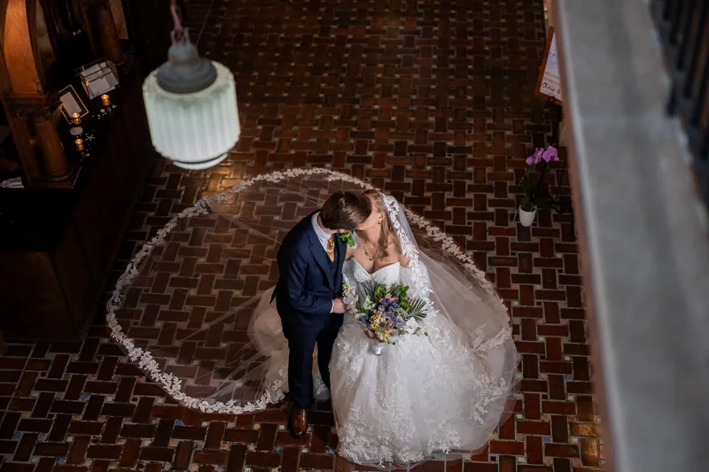 Sybil and Chris stand together on a decorative floor at The Treasury on the Plaza, Sybil in a white gown and Chris in a dark