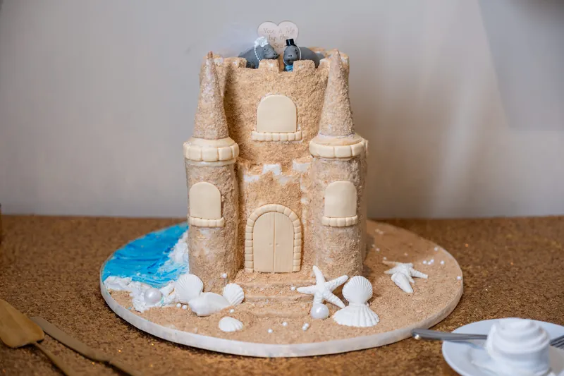 A sand-colored castle cake with turrets and decorative elements displays the couple's shoes at the top, surrounded