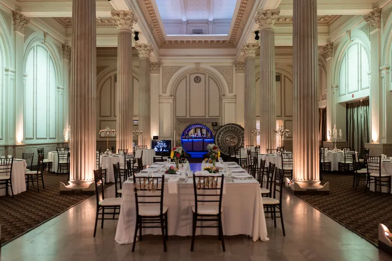 Elegant ballroom at The Treasury on the Plaza features crisp white linens, black chiavari chairs, and soaring columns bathed