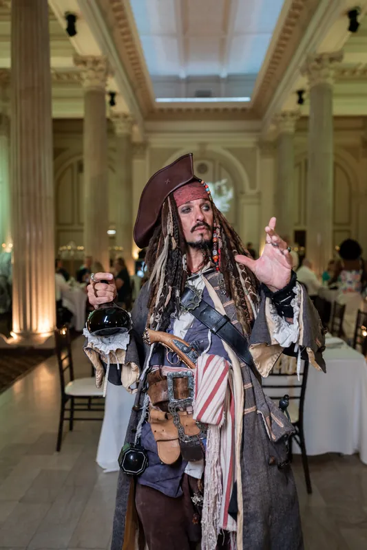 A performer in full Captain Jack Sparrow costume gestures expressively during the reception, entertaining guests inside