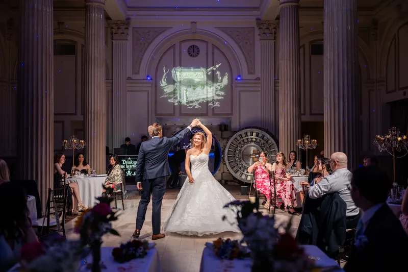 Chris dips Sybil during their first dance as guests watch from the columned ballroom floor beneath an arched ceiling.