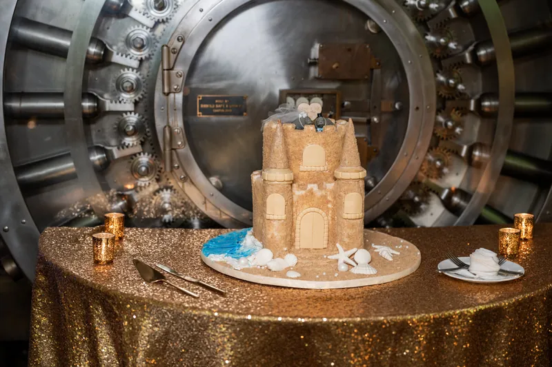 Sand-colored castle cake with seashell decorations sits before a massive vintage bank vault at The Treasury on the Plaza.