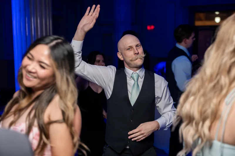 A guest raises his arm while dancing as Sybil smiles nearby during the reception.