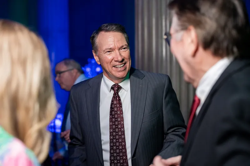 A man in a gray suit chats with another guest, smiling broadly at The Treasury on the Plaza.