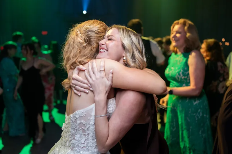 Sybil embraces a guest warmly on the dance floor as others look on in the background.
