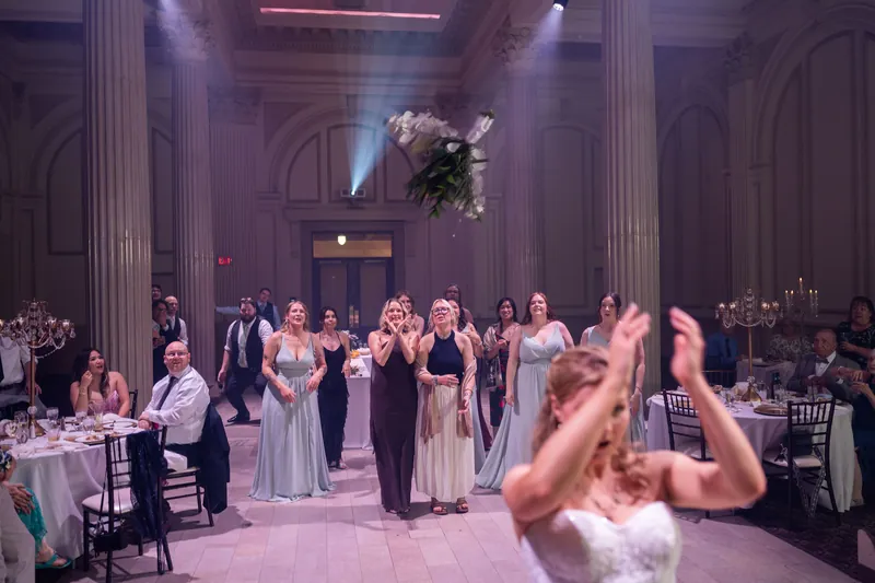 Sybil tosses her bouquet to guests gathered in the illuminated hall at The Treasury on the Plaza as attendants watch