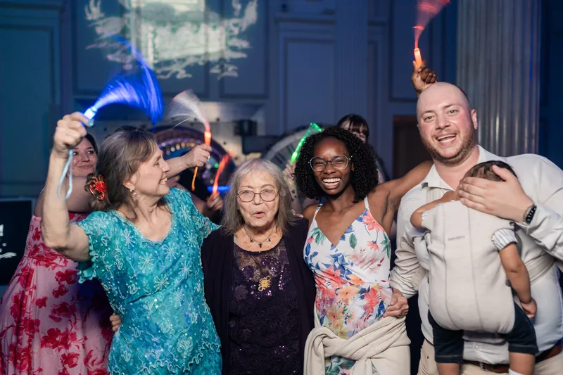 A group of five family members pose together indoors, smiling at the camera with festive props including a blue top hat.