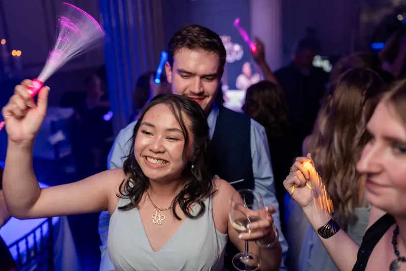 Sybil holds a champagne flute and beams while dancing with guests under blue stage lighting at The Treasury on the Plaza.