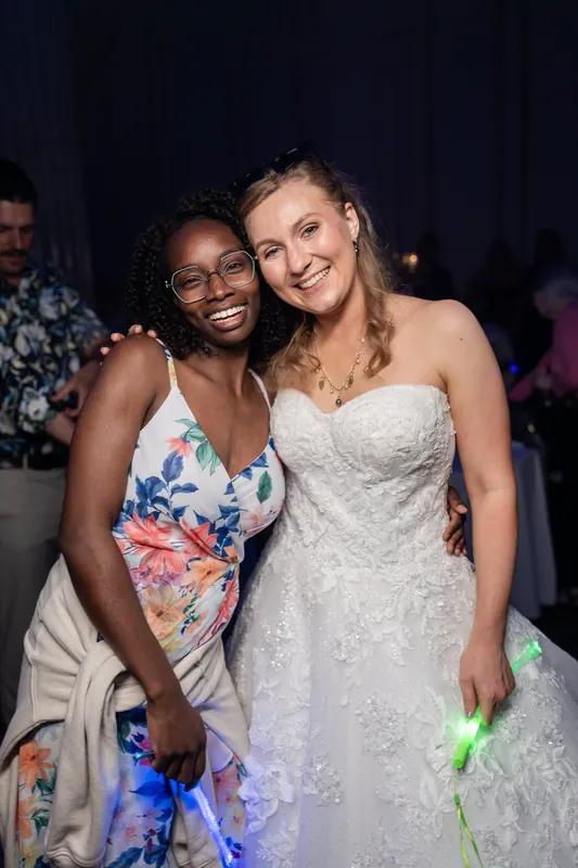 Sybil in a beaded white gown smiles beside a guest in a colorful floral dress at The Treasury on the Plaza.