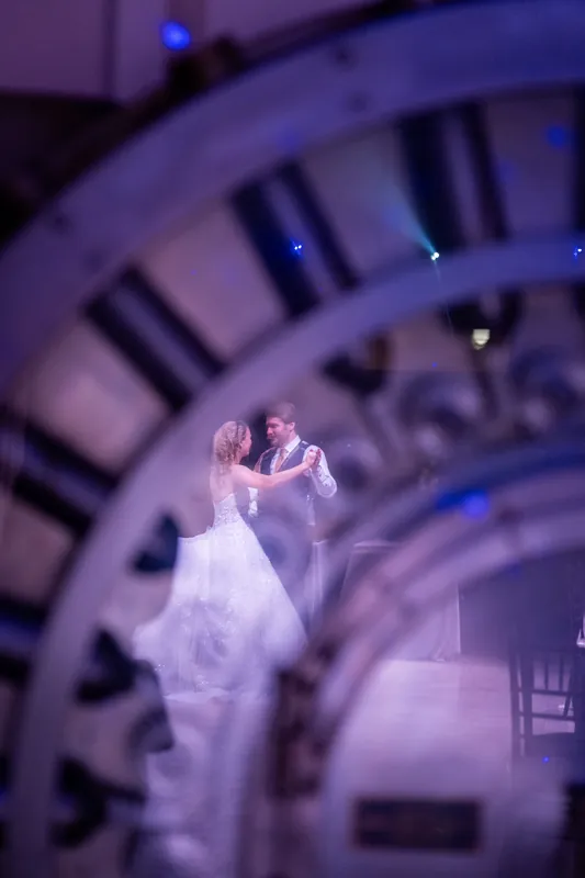 Sybil twirls in her white gown beneath an ornate clock face glowing in purple light.