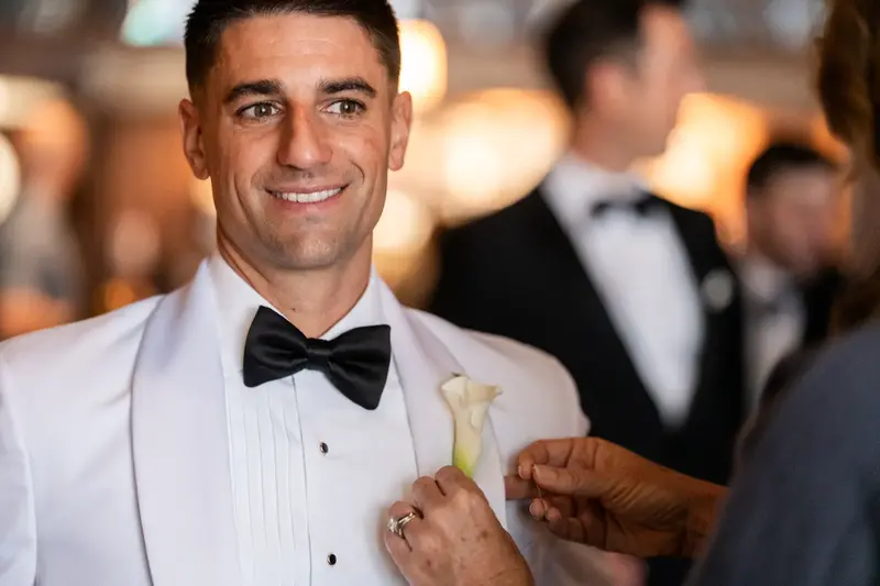 Jay getting his boutonniere pinned on before the ceremony in white dinner jacket
