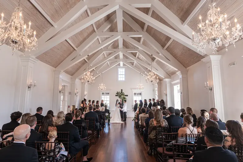 Wide ceremony view in white chapel with vaulted ceiling and crystal chandeliers