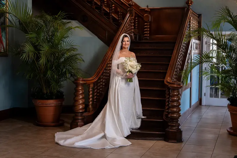 Tayler on grand staircase holding bouquet with palm plants