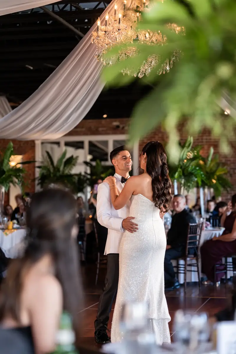 First dance framed through palm fronds with chandelier above