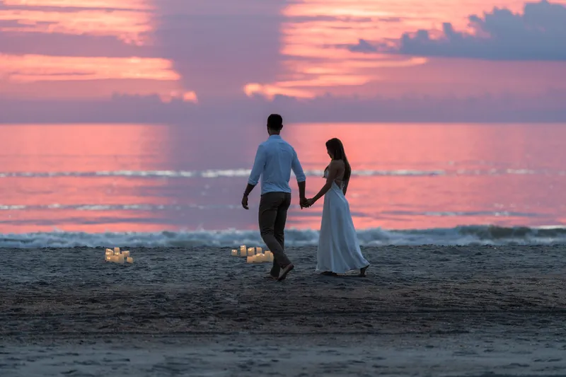 Thomas and Colleen walk hand in hand along Vilano Beach at sunset under a pink and purple sky.