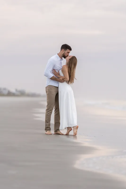 Thomas kisses Colleen on the beach as waves lap at the shore, the couple embracing in the wet sand.