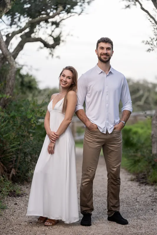 Colleen smiles beside Thomas under a sprawling oak tree on a sandy path at Vilano Beach.