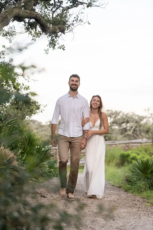 Thomas and Colleen walk hand-in-hand down a tree-lined dirt road with palmetto vegetation at Vilano Beach.