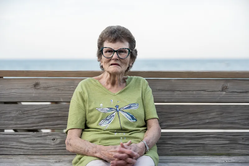 Woman in lime green dragonfly shirt sits on wooden bench facing the ocean at St. Augustine Beach.
