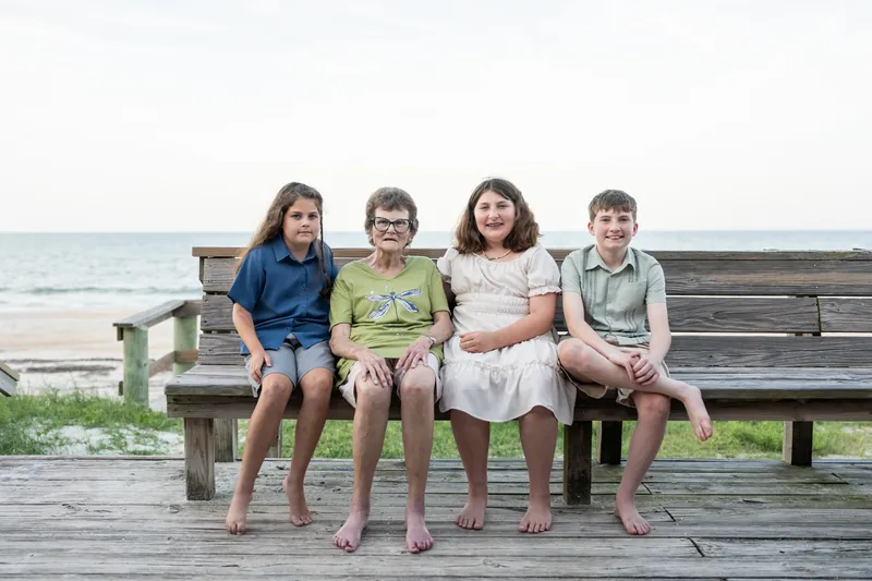 Four children sit barefoot on a wooden bench overlooking the ocean at St. Augustine Beach.