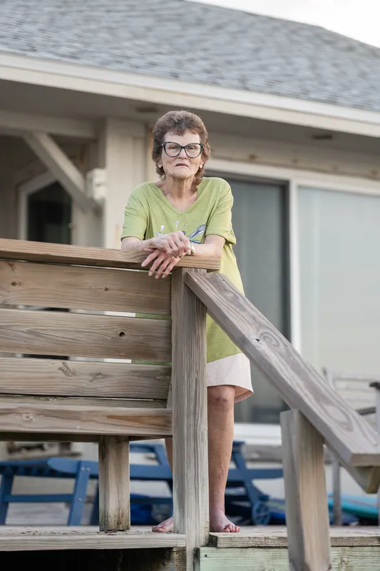 Girl wearing glasses and a lime-green top leaning on a wooden deck railing.