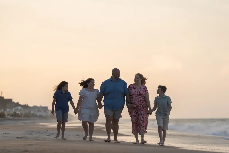 Five family members stand together at St. Augustine Beach during golden hour, facing the calm ocean waves.