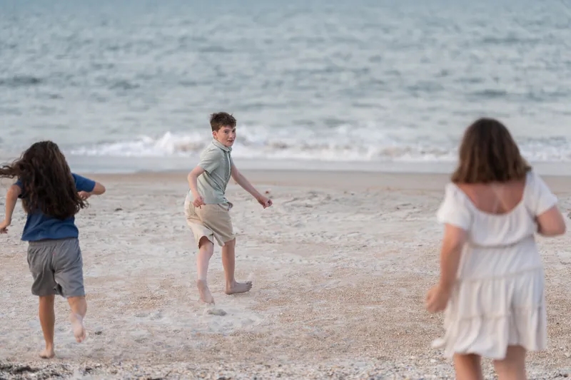 Three children run and play together in the shallow surf at St. Augustine Beach.
