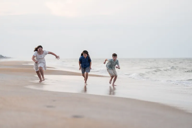 Three children splash through the wet sand and water at St. Augustine Beach, racing toward the waves.