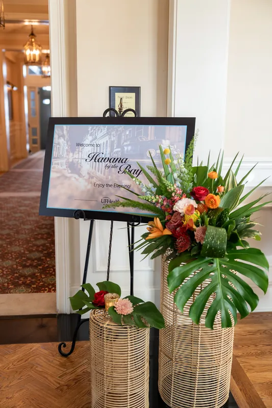 Welcome sign with red and orange floral arrangement in woven baskets at River House Events' entrance, St. Augustine.