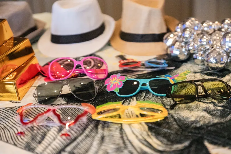 Photo booth props including Panama hats, colorful sunglasses, and sparkly accessories on a table at River House Events.