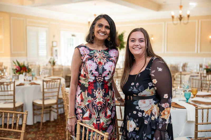 Two women in floral and patterned dresses smile together in the elegant ballroom at River House Events.