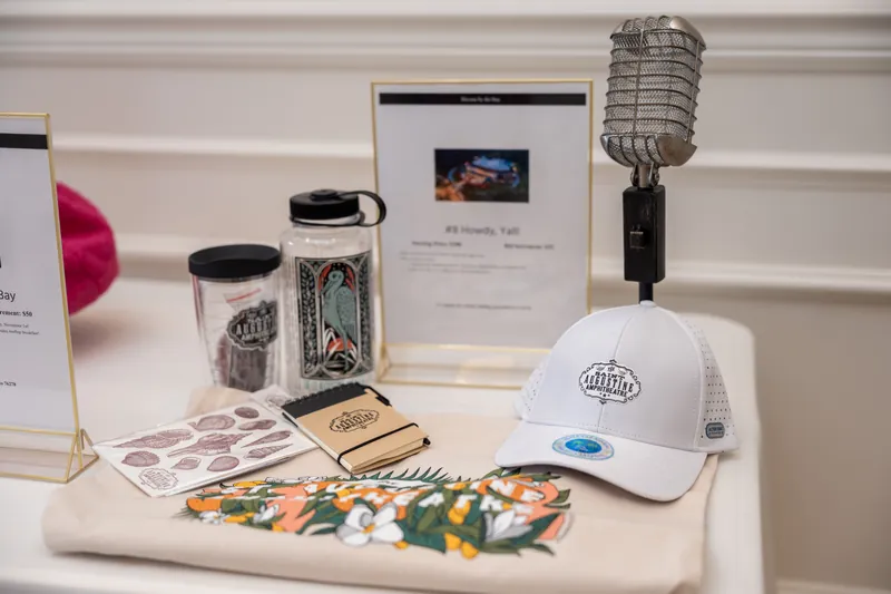 Vintage microphone, UF-branded tumblers and cap, and printed materials arranged on a white table at River House Events.