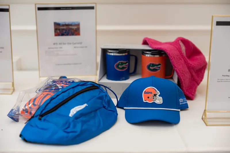 Blue and orange UF caps, drinkware, and a bright pink fabric accent displayed on a white surface.