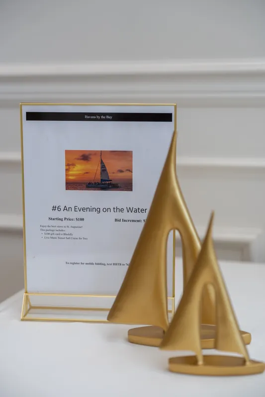Gold sailboat sculptures flank a framed description of an evening on the water, displayed at River House Events.