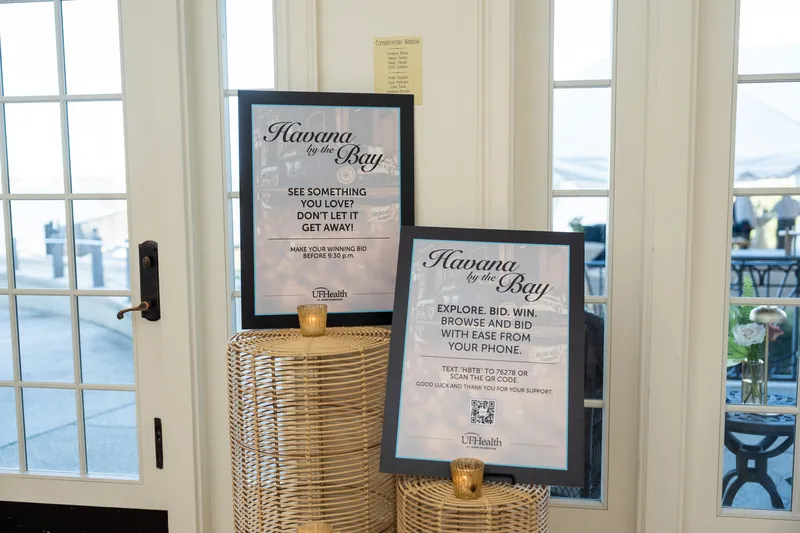 Two framed event cards on woven pedestals near tall windows overlooking the waterfront.