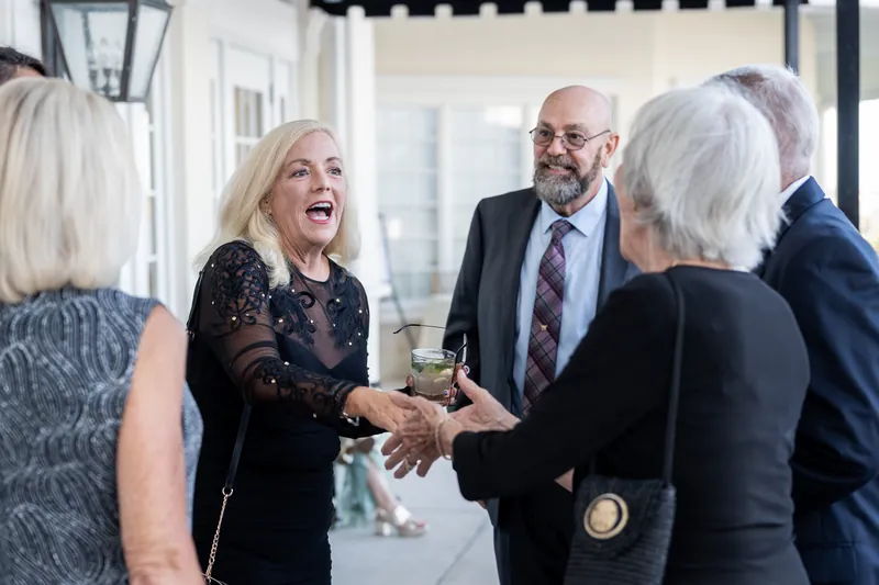 Two people shake hands and laugh while others join at River House Events, St. Augustine.