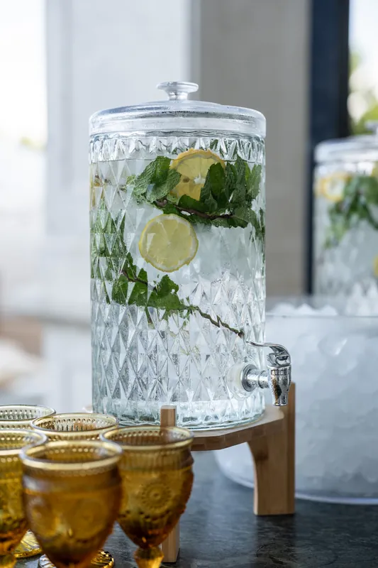 Crystal beverage dispenser with lemon slices and mint sits beside gold cocktail glasses.