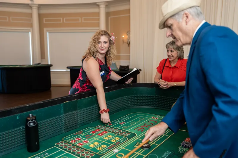 Woman in a fuchsia dress places a bet at a roulette table while a man in blue watches nearby.