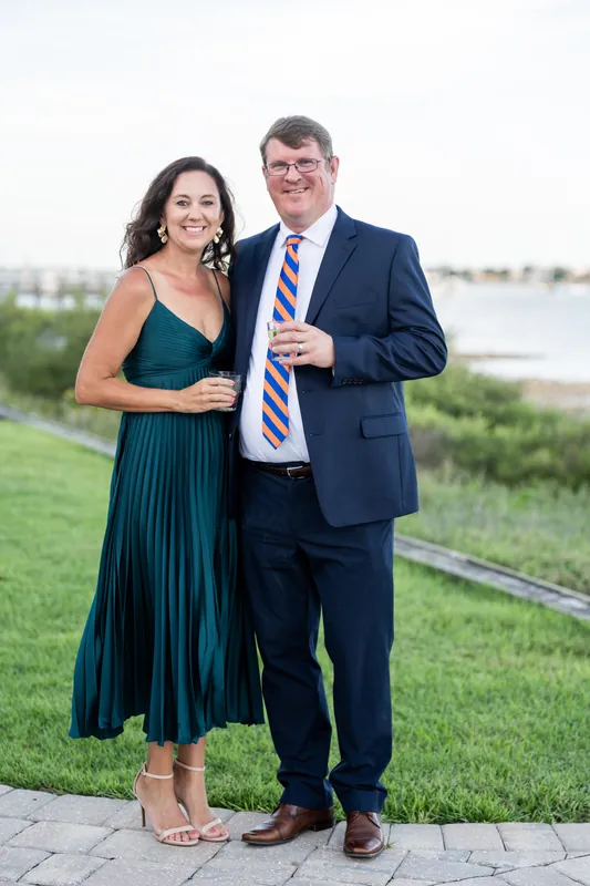 Two people in formal attire pose on the grass with the river visible behind them at River House Events.