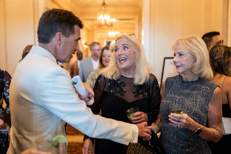 Three guests converse and smile while holding drinks in the warmly lit interior at River House Events, St. Augustine.